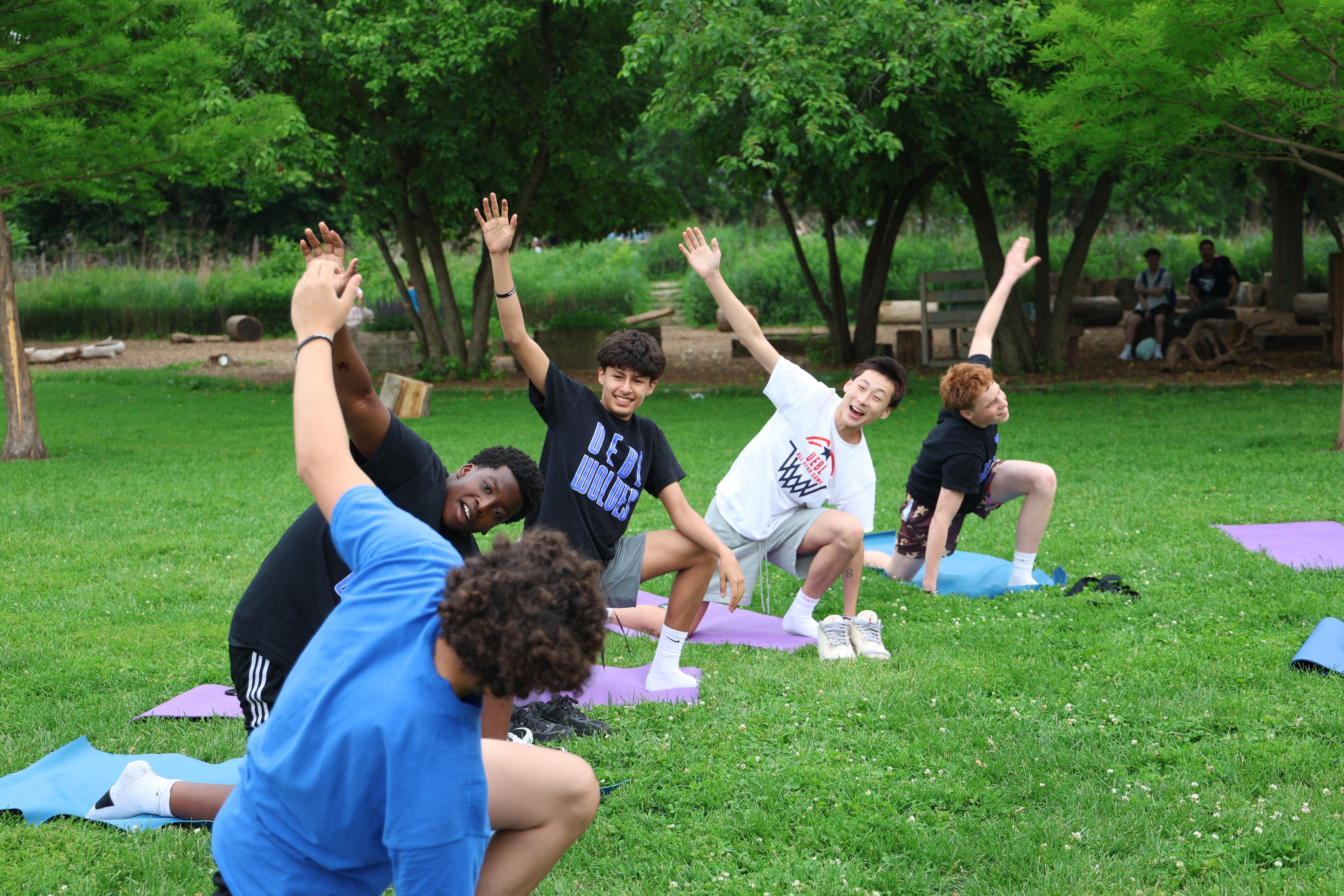Teenagers practice yoga on mats in a grassy park.